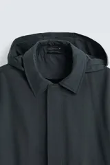 Parka larga color verde oscuro, con capucha desmontable, cuello solapa, bolsillos laterales y cierre frontal con cremallera oculta y botones a presión. Incluye chaleco interior acolchado desmontable.