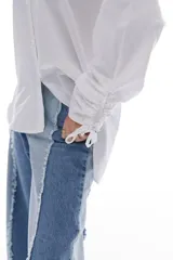 Camisa blanca de algodón con cuello clásico, mangas largas con puños fruncidos y cierre de botones al frente. Presenta frunces y lazo ajustable en la espalda.