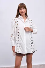 Camisa blanca de corte recto, con cuello clásico, cierre frontal con botones y mangas largas. Presenta apliques de encaje calado en los laterales del frente y en las mangas.