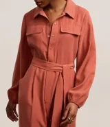 Mono largo color ladrillo, de corte sastrero, con cuello camisero, cierre frontal con botones y cinturón de lazo en la cintura.