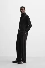 Pantalón negro de corte amplio, con pliegues frontales, bolsillos laterales y traseros de ojal. Incluye cinturón de la misma tela con hebilla metálica.