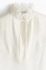 Blusa blanca de corte holgado en tejido transparente de mezcla de lyocell. Modelo de manga larga con cuello elevado de encaje, puños anchos abotonados y bajo recto. Pechera con abertura, alforzas y tiras spaghetti.