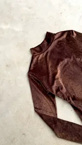 Body de terciopelo marrón con estampado de piel de serpiente, cuello alto, mangas largas con orificio para el pulgar y espalda descubierta.