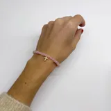 Pulsera elástica con cuentas de cuarzo rosa y dije de cruz dorada con incrustaciones brillantes.