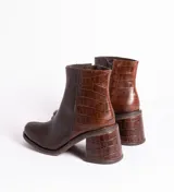 Bota corta de cuero marrón con detalle de cuero con textura de cocodrilo en el lateral y en el taco. Tiene cierre del lado interno y taco de madera forrada en cuero de 7cm.