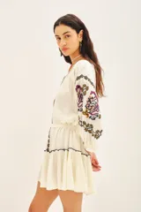 Vestido corto de bambula color celeste claro con bordados florales multicolor en el frente y mangas. Presenta escote redondo con cartera, cinturón de tela ajustable y volado en el ruedo.