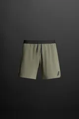 Shorts deportivos color verde oliva confeccionados en tejido técnico ligero y elástico con forro interior. Presentan cintura elástica ajustable con cordón, bolsillos laterales, bolsillo de seguridad en la espalda con cierre de cremallera, bajo con aberturas laterales y logo estampado en la pierna.