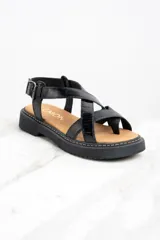 Sandalia de cuero color negro charol, con tiras cruzadas y hebilla ajustable al tobillo. Plataforma con suela track.