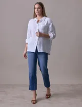 Camisa blanca de algodón con textura arrugada, cuello con solapa, abertura central con botones y bolsillo aplicado en el pecho. Mangas largas con largo regulable mediante presilla y botón.