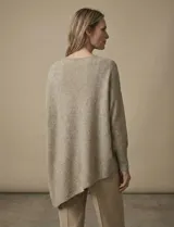 Poncho de tejido lurex color verde oliva con brillo sutil, de corte amplio y manga larga con puños acanalados. Presenta un bajo asimétrico con caída diagonal.