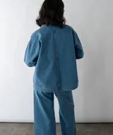 Camisa celeste de denim con cuello clásico, mangas largas con puños abotonados, cierre frontal con botones a presión y dos bolsillos de parche en el pecho.