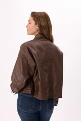 Campera corta color beige claro, estilo bomber o trucker, confeccionada en símil cuero suave. Presenta cuello mao, cierre frontal metálico, bolsillos frontales con tapa y botones a presión, y reguladores ajustables en el ruedo.