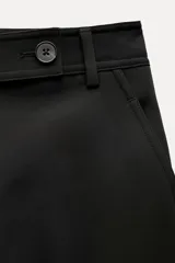 Pantalón negro de tiro medio, con trabillas en la cintura, bolsillos laterales y de vivo en la espalda, raya planchada en el delantero y pierna recta.