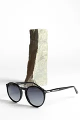 Lentes de sol unisex con montura redonda negra y lentes degradadas de gris a transparente.