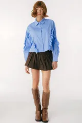 Camisa celeste con cuello clásico, cierre frontal con botones y mangas largas con volados.