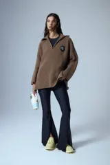 Sweater marrón de punto con cuello polo, cierre de cremallera parcial y parche bordado en el pecho.