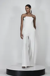 Mono strapless blanco de sastrería con recortes metálicos en el escote, costuras estratégicas y pierna ancha.