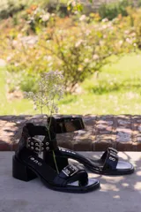 Sandalia de cuero negro con hebilla doble en el talón y taco cuadrado.