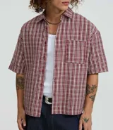 Camisa de manga corta con cuello inglés, corte oversized y estampado de cuadros en tonos rojo, blanco y negro.