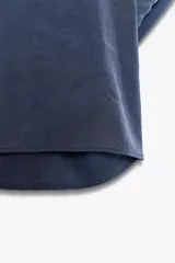 Camisa azul de cuello solapa y manga corta con dobladillo. Tiene dos bolsillos de parche en el pecho, bajo asimétrico con aberturas laterales y cierre frontal con botones ocultos.
