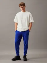 Pantalón de chándal azul eléctrico de felpa de algodón regenerativo, con cintura elástica con cordón, puños de canalé, bolsillos laterales y trasero, y logo de Calvin Klein en relieve en la cadera.