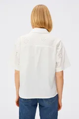 Camisa blanca de algodón con bordado calado de flores, cuello camisero, corte recto y mangas cortas.