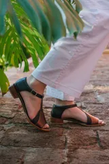 Sandalias de cuero color blanco con detalles dorados, taco bajo de madera y tira con hebilla al tobillo.