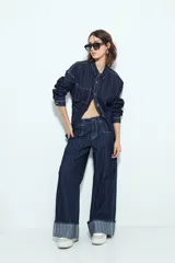 Pantalón de jean de tiro bajo, color azul oscuro, con rayas verticales blancas y silueta ancha (wide leg). Presenta costuras contrastantes y dobladillo ancho doblado hacia afuera.