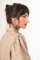 Camisa beige de efecto piel con cuello clásico, mangas largas abullonadas y cierre frontal con botones a tono.