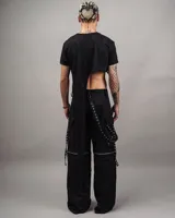 Pantalón negro de corte holgado con múltiples correas y ojalillos metálicos.