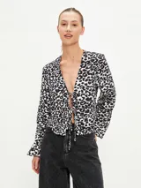 Blusa negra con estampado animal print en blanco y marrón, escote en V con lazo ajustable y mangas largas acampanadas.