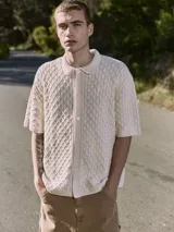 Polo de hombre color crema, tejido de punto cable, con cuello tipo polo, manga corta y cierre con botones.