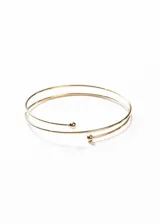 Brazalete dorado de acero quirúrgico hipoalergénico, con diseño abierto y ajustable, y terminaciones en forma de esfera.