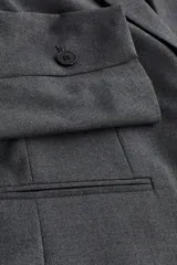 Blazer entallado gris con solapas de muesca y cierre de un botón. Tiene bolsillos ribeteados en el frente, botones decorativos en los puños y abertura en la parte posterior.