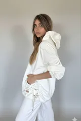 Canguro oversize color blanco, con capucha, cordones ajustables, mangas 3/4 con puños elásticos, bolsillos laterales y ruedo irregular con cordones ajustables.