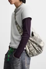 Bolso de hombro color gris con efecto desgastado, fabricado en tejido de algodón. Tiene un compartimento principal con cierre de cremallera, un bolsillo interior con cremallera y asa de hombro ajustable.