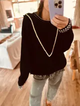 Sweater negro de punto con cuello redondo, mangas largas y ribete blanco en cuello y mangas. Presenta detalle de bordado con pompones blancos en forma de V en el frente.