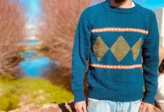 Sweater de lana color azul con cuello redondo y diseño intarsia de rombos color ocre y rayas horizontales color naranja.