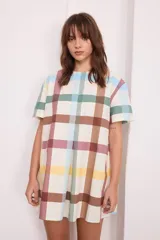 Vestido corto de algodón a cuadros color crema, verde y borgoña, con cuello redondo y mangas cortas. Presenta tablas en la parte delantera y trasera.