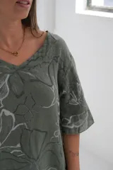 Blusa verde con estampado de flores blancas, cuello en V y mangas cortas.