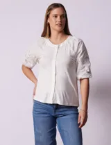 Blusa blanca de cuello redondo con apertura central y botones. Mangas 3/4 con detalle de bordado calado.