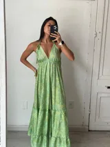Vestido largo de seda verde con estampado paisley en tonos amarillos y blancos. Tiene escote halter con tirantes finos que se atan al cuello y espalda descubierta. La falda es amplia y con volantes en el ruedo.