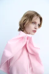 Camisa de popelín rosa de algodón, con cuello solapa, manga larga con puños plisados y volumen en un hombro. Cierre frontal con botones ocultos.
