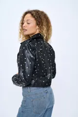 Chaqueta corta estilo motoquera de cuero sintético negro, con cuello solapa y cierre cruzado con cremallera. Decorada con tachas plateadas en solapas, hombros y mangas.