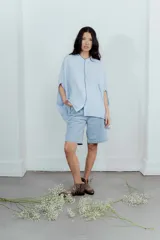 Camisa celeste de lino con corte amplio, cuello mao y mangas cortas. Presenta cierre frontal con botones y ribete negro en cuello y tapeta.