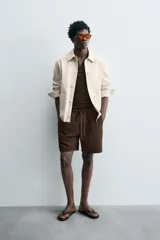 Bermuda de algodón color marrón oscuro, de corte regular fit, con cintura elástica ajustable mediante cordón. Presenta bolsillos laterales y un bolsillo trasero de vivo.