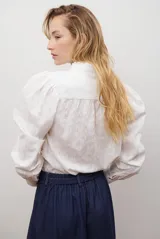 Camisa azul marino con estampado floral en color lila, cuello mao con volantes, cierre frontal de botones y mangas largas abullonadas con puños elásticos.