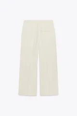 Pantalón negro de tiro alto con trabillas, bolsillos laterales y pinzas. Cierre frontal con cremallera, botón interior y gancho metálico.