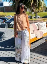 Pantalón de lino blanco con estampado floral en tonos beige y verde, de corte palazzo.