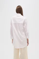 Camisa blanca de algodón con cuello clásico, corte holgado, cierre frontal con botones y mangas largas.